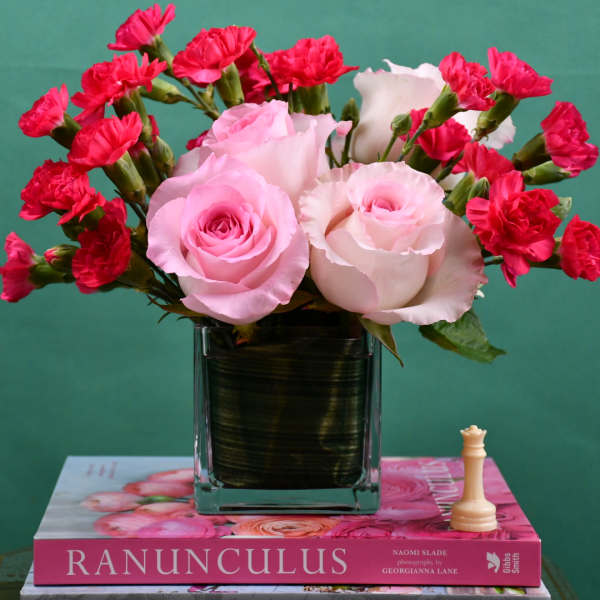 Pink roses and red carnations in a square glass vase on a book
