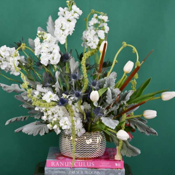 Tall white floral arrangement in a patterned vase with tulips and spiky blue accents