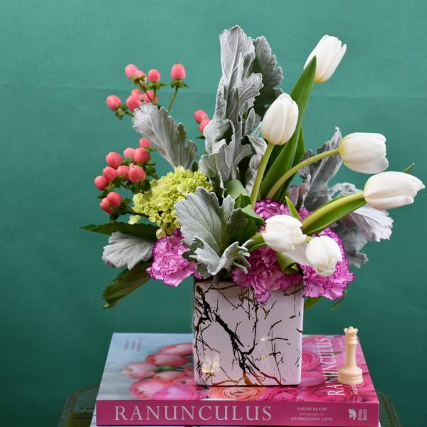 White tulips and pink flowers in a patterned square vase