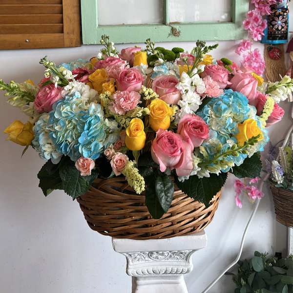 Basket arrangement of pink, yellow, and blue flowers on a pedestal
