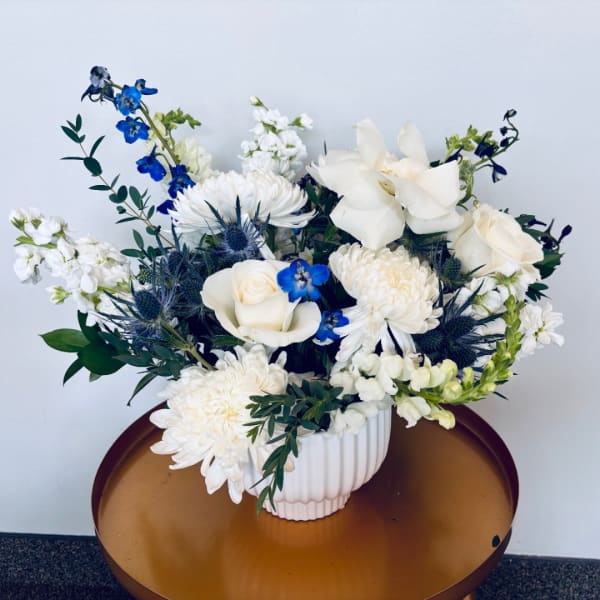 White and blue floral arrangement in a ribbed white vase