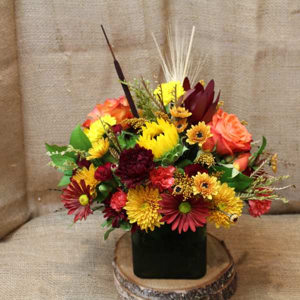 Mixed bouquet of red, orange, and yellow flowers in a dark square vase