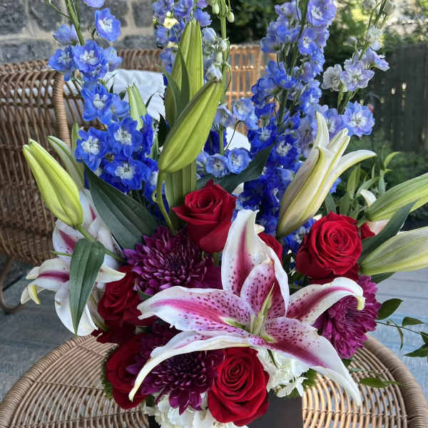 Bouquet of red roses, pink lilies, and blue delphinium in a black box