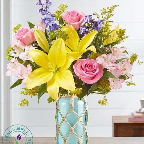 Bouquet of pink roses, yellow lilies, and purple flowers in a blue vase