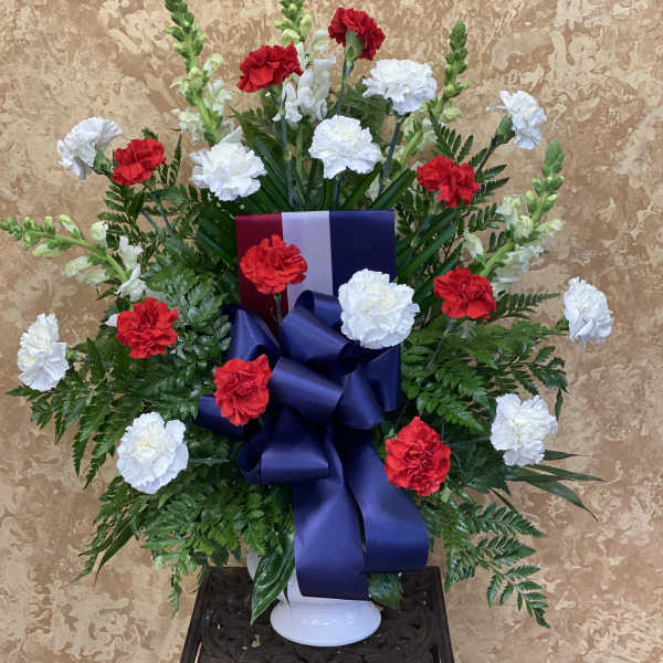 Red and white carnations in a white vase with a large blue ribbon