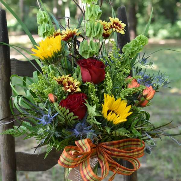 Mixed bouquet of red roses, yellow blooms, and blue thistle in a glass vase
