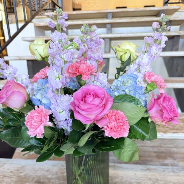 Pink roses, lavender blooms, and blue hydrangeas in a glass vase