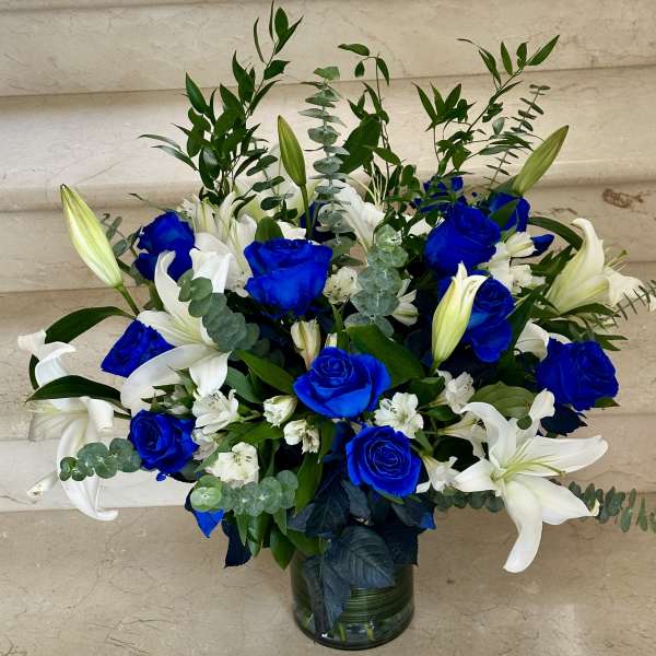 Blue roses and white lilies in a glass vase with greenery