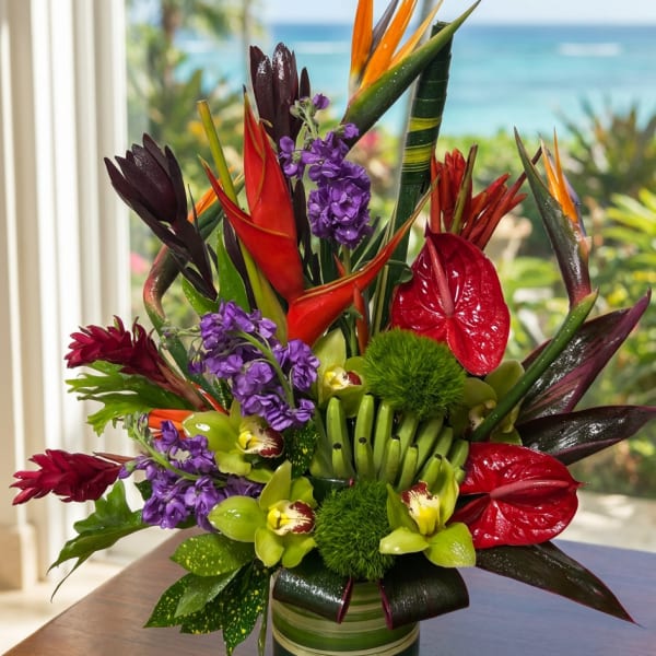 Tropical arrangement with red anthuriums, purple flowers, and bird of paradise in a striped vase.