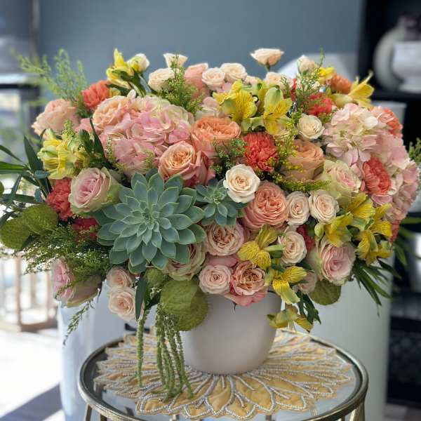 Large pastel bouquet in a white vase with roses, hydrangeas, and succulents