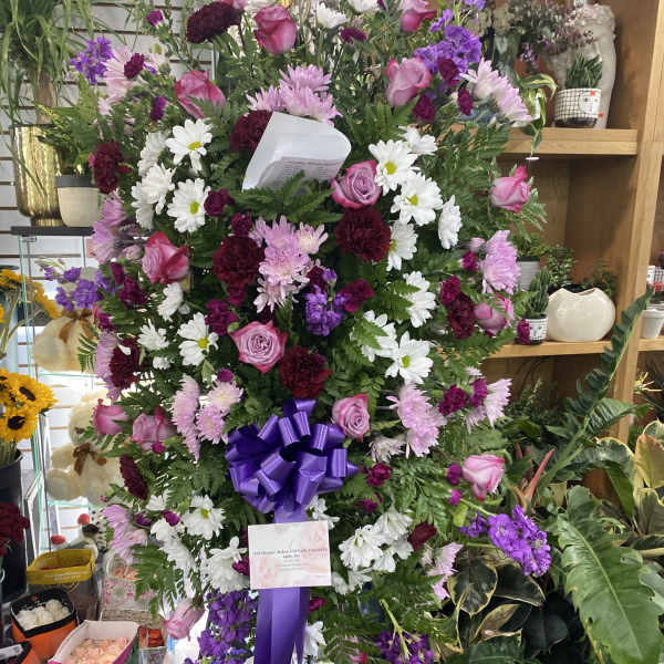Large standing spray of pink, white, and purple flowers with a purple ribbon