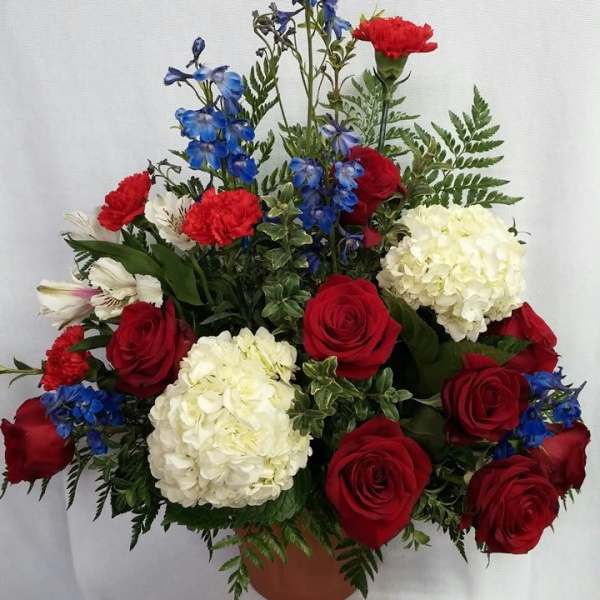 Red roses, white hydrangeas, and blue flowers in a terracotta pot