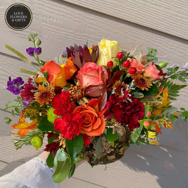 Low arrangement of red and orange roses and carnations with yellow accents in a rustic basket