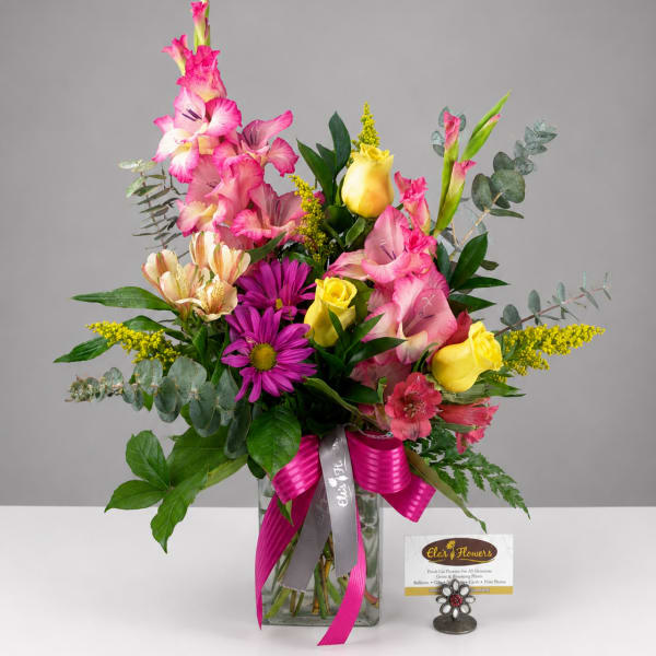 Mixed bouquet with pink gladiolus, yellow roses, and purple daisies in a glass vase