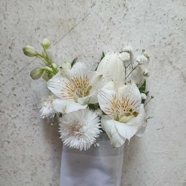 White floral corsage with lilies and small white blooms on a ribbon wrap
