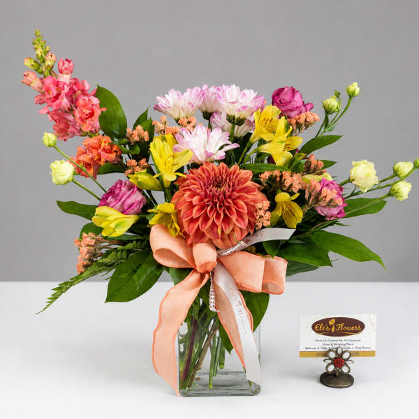 Colorful mixed bouquet in a clear glass vase with a peach ribbon