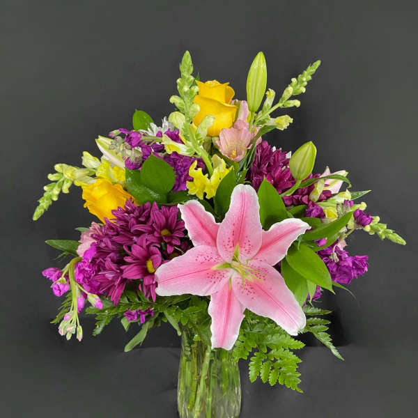 Pink lily and mixed purple-yellow flowers in a clear glass vase