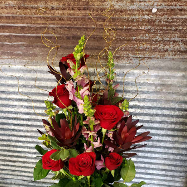 Tall arrangement of red roses and pink snapdragons in a burgundy vase