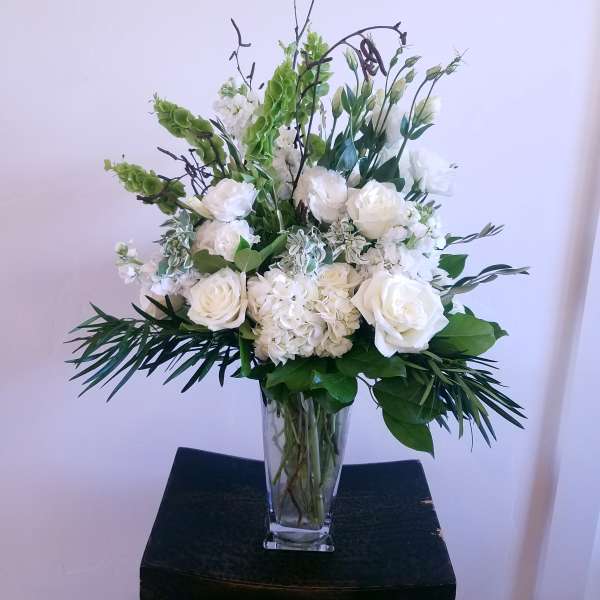 White floral arrangement in a clear glass vase with tall greenery