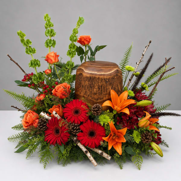 Autumn floral arrangement with orange roses, red gerberas, lilies, and a wooden urn