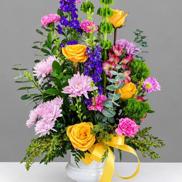 Tall mixed bouquet in a white vase with yellow roses, purple flowers, and pink blooms