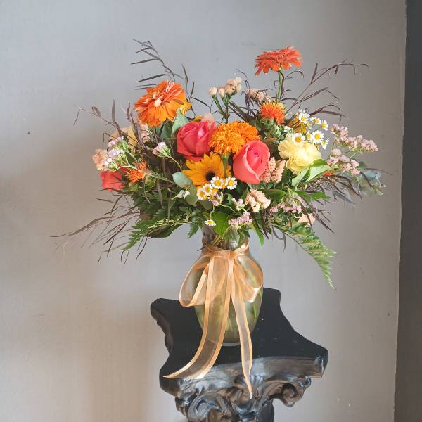 Mixed bouquet of orange, pink, and white flowers in a glass vase with ribbon