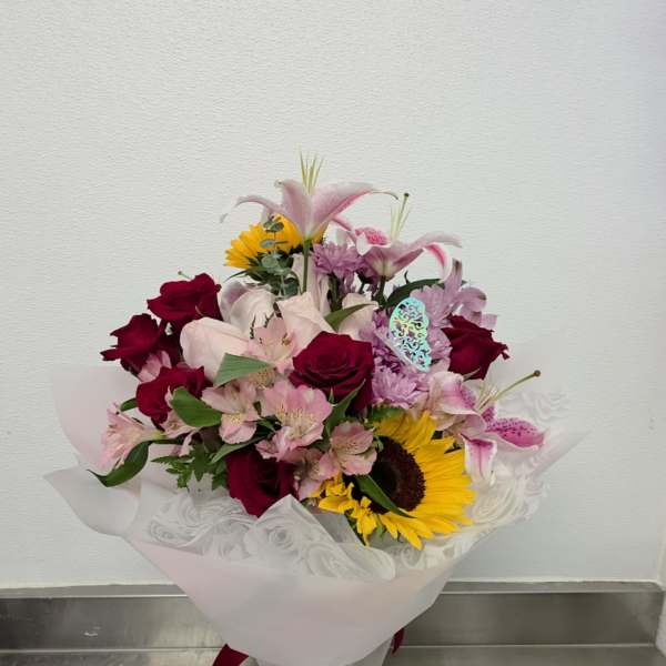 Mixed bouquet of roses, lilies, and a sunflower in a glass vase