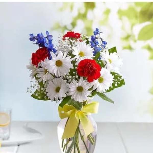Bouquet of red, white, and blue flowers in a glass vase with a yellow ribbon