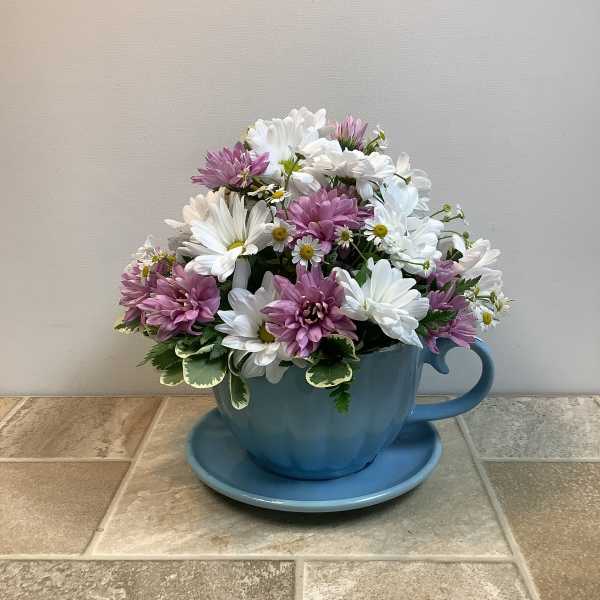 Pink and white daisy bouquet in a blue teacup planter