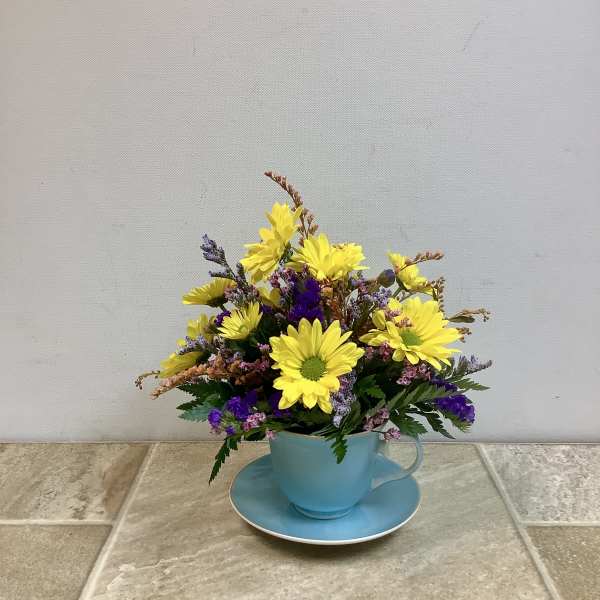 Yellow and purple flowers arranged in a blue teacup with saucer