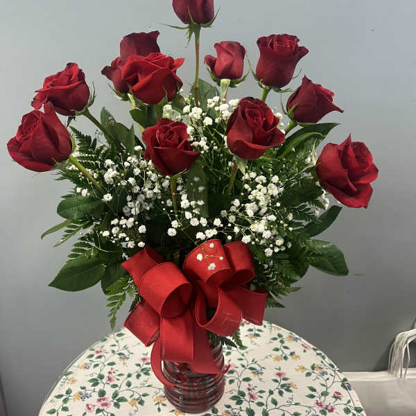 Red roses in a glass vase with baby's breath and a red ribbon