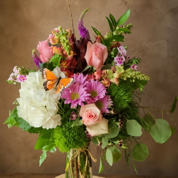 Mixed bouquet of pink and white flowers in a glass vase with a butterfly accent