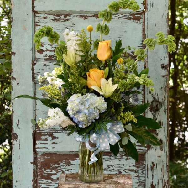 Bouquet of yellow roses, hydrangea, and white lilies in a glass vase