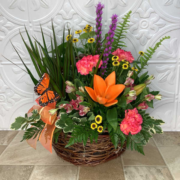 Basket arrangement with orange lilies, pink carnations, and a butterfly decoration