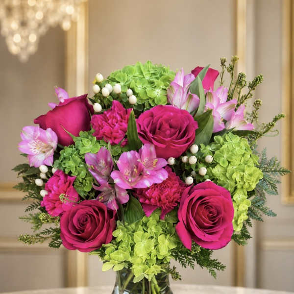 Pink roses and alstroemeria arranged with green hydrangea in a glass vase.