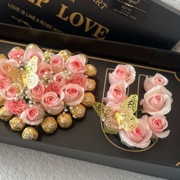 Pink roses and chocolates arranged in a black gift box with butterfly decorations.