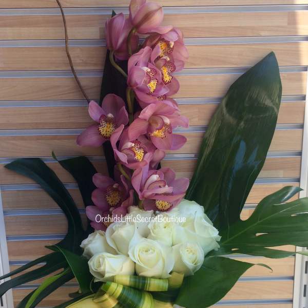Pink orchids and white roses in a clear glass vase with large tropical leaves