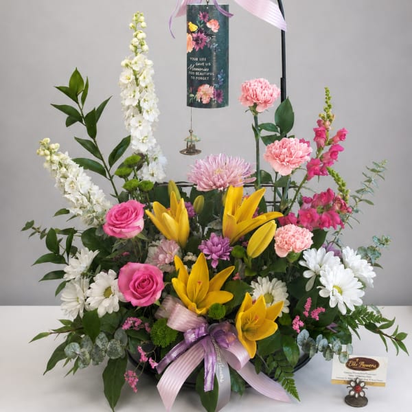 Standing floral sympathy arrangement with lilies, roses, and daisies on a black easel