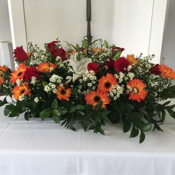 Large floral centerpiece with red roses, orange gerbera daisies, and white lilies