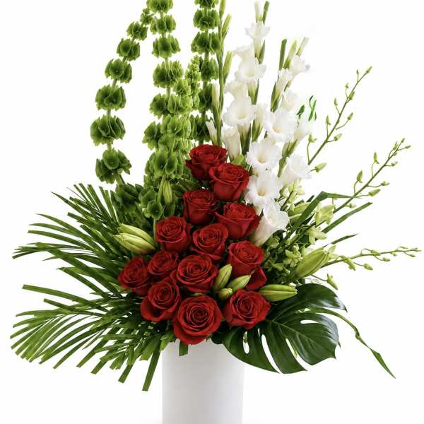 Red roses and white orchids in a white vase with tall green accents