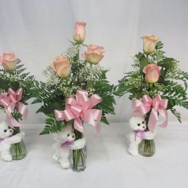 Three pink rose arrangements in glass vases with teddy bears and ribbons