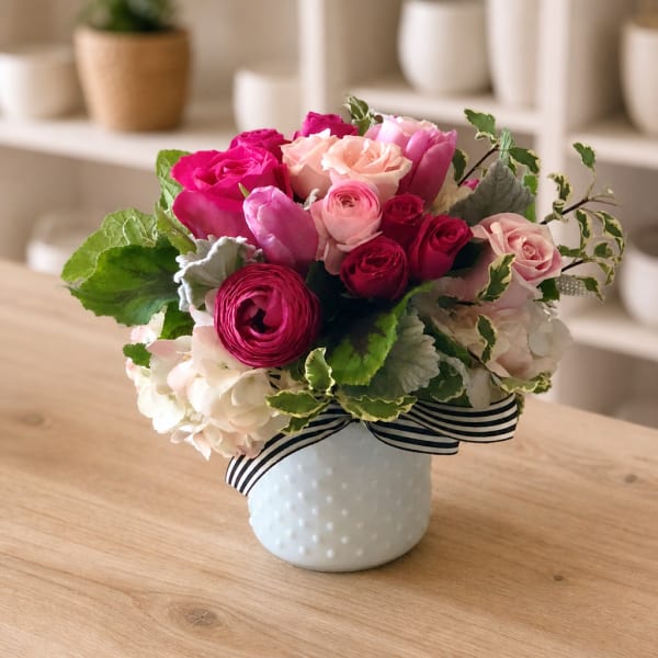 Pink and peach rose bouquet in a white vase with a striped ribbon