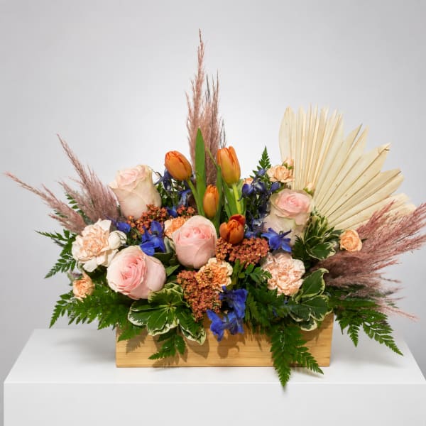 Mixed bouquet with pink roses, orange tulips, and blue flowers in a wooden box