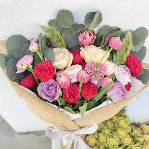 Bouquet of pink, cream, and lavender flowers wrapped in burlap with a ribbon