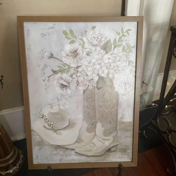 Framed artwork of white flowers in a vase beside a cowboy hat and boots