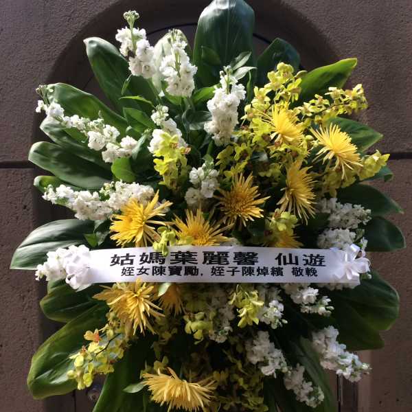 Standing floral wreath with yellow and white flowers and a condolence ribbon