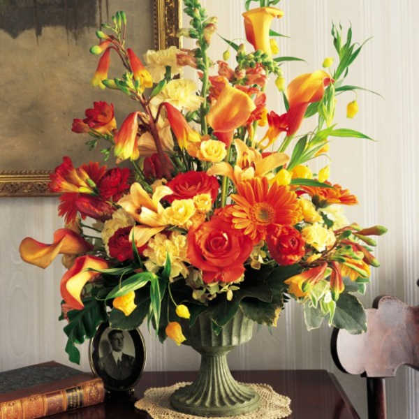 Tall arrangement of orange, yellow, and red flowers in a green pedestal vase
