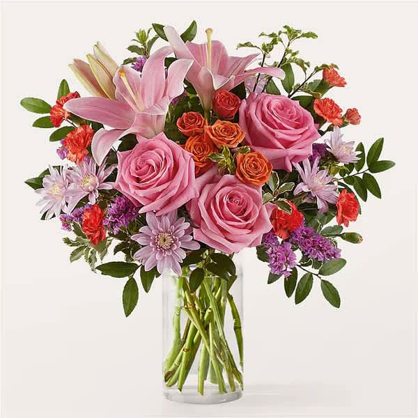 Pink roses and lilies arranged in a clear glass vase