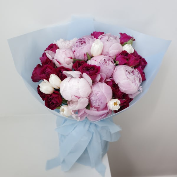 Bouquet of pink peonies and dark red roses wrapped in pale blue paper
