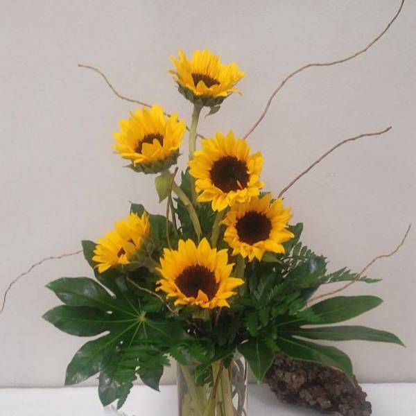Sunflower arrangement in a clear glass vase with decorative figurines